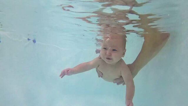 Shocked and puzzled baby girl dives into water with parent help. Excited daughter explores underwater with amused and confused expression
