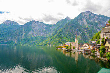 Fototapeta na wymiar Famous view of Hallstatt city and church near the lake. Mountains in the background. Summer rainy day, soft colors, cloudy weather.