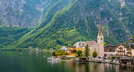 Fototapeta na wymiar Famous view of Hallstatt city and church near the lake. Mountains in the background. Summer rainy day, soft colors, cloudy weather.