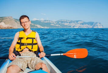 A young man is sailing on a kayak on the sea against the backdrop of mountains close-up, front view