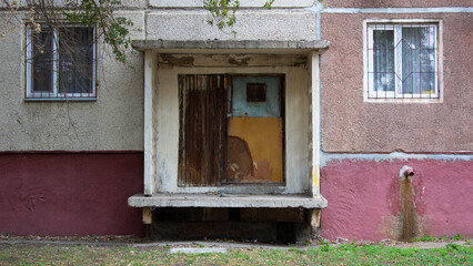 The entrance of house raised above the ground in Kazakh city of Pavlodar. Abandoned and closed entrance to house. Square portal with a rain canopy without a ladder. The concept of decline and ruin