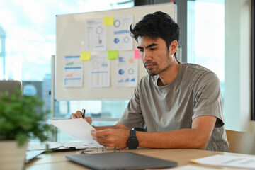 Fototapeta na wymiar Focused start up businessman checking financial reports on working desk in modern office