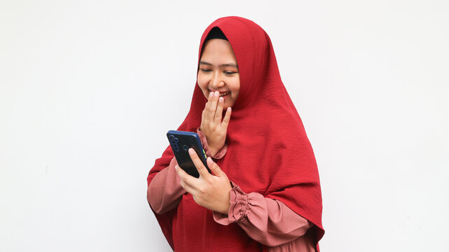 Lovely happy smiling asian woman wearing red hijab looking on smartphone over isolated white background