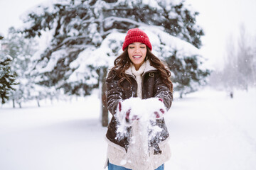 Fototapeta na wymiar Happy young woman plays with a snow in sunny winter day. Walk in winter forest. Christmas, holidays concept.