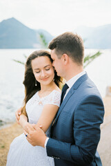 Groom hugs the bride, who closed her eyes by the shoulders on the seashore. Portrait