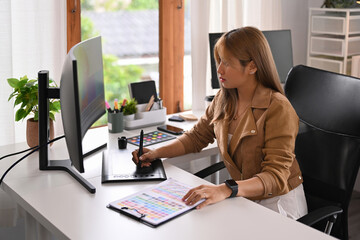 Asian female freelance graphic designer using digital tablet for making new designs, working at home office