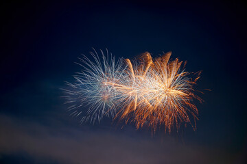 Close up of fireworks explosion with white and orange stars. Isolated on black and blue night sky. Ideal for Sylvester and New Year.