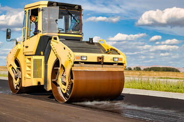 Vibratory road roller lays asphalt on a new road under construction. Close-up of the work of road machinery. Construction work on the construction of urban highways.