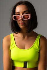 Sport girl pink glasses and neon colour swimsuit posing and showing legs and back in studio, stylish and trendy photoshoot