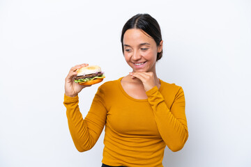 Young hispanic woman holding a burger isolated on white background looking to the side and smiling