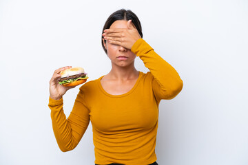 Young hispanic woman holding a burger isolated on white background covering eyes by hands. Do not want to see something