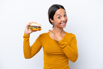 Young hispanic woman holding a burger isolated on white background pointing to the side to present a product