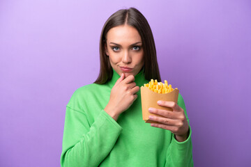 Young caucasian woman holding fried chips on purple background thinking