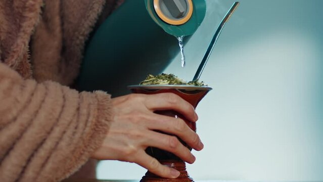 Mate drink. Person pours hot water in the traditional cup with mate drink