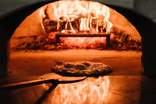The chef takes a baked pizza Margherita, four cheese or meat pizza from the oven. A cooking and baking pizza in a firewood oven. Italian traditional pizza is cooked in a stone wood-fired oven.