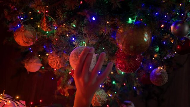 Boy decorating Christmas tree with beautiful ornaments and baubles at home