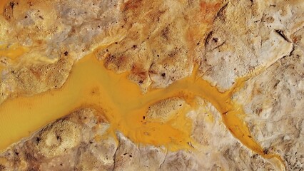 Lifeless orange toxic river near green trees. Industrial plant pollutes soil and forest. Aerial view, drone flying