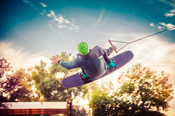 A guy in a yak suit at sunset jumps from a springboard on a wakeboard in an extreme park in Kiev....