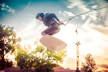 A guy in a yak suit at sunset jumps from a springboard on a wakeboard in an extreme park in Kiev....