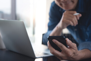 Close up of asian casual business man using mobile phone and working on laptop computer with digital tablet on office table