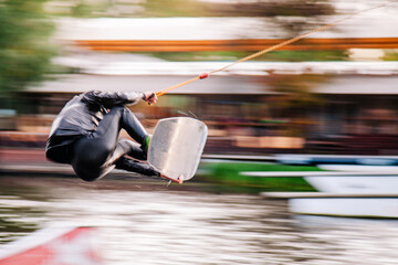 A guy in a yak suit at sunset jumps from a springboard on a wakeboard in an extreme park in Kiev....