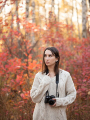 Beautiful young woman standing in autumn forest with dslr camera