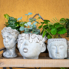 artificial flowers in stone vases in the form of heads of idols on a shelf as an interior decoration