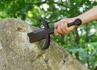 hand of the knight who tries to extract the Excalibur Sword stuck in the rock in the middle of the forest