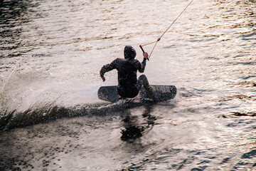 A guy in a yak suit at sunset jumps from a springboard on a wakeboard in an extreme park in Kiev. Ukraine.