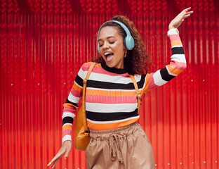 Dance, music and freedom with a black woman on a red background outdoor for fun or movement. Radio, streaming and audio with a young female dancing while listening to a playlist on headphones © Kay Abrahams/peopleimages.com
