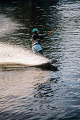 A guy in a yak suit at sunset jumps from a springboard on a wakeboard in an extreme park in Kiev....