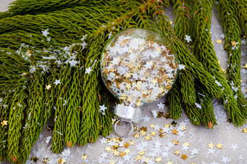 Christmas tree leaf with bauble filled with star confetti on gray with snow and stars