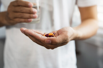 male hand holding pills and glass of water male taking pills Discomfort health care concept.