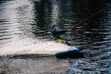 A guy in a yak suit at sunset jumps from a springboard on a wakeboard in an extreme park in Kiev....