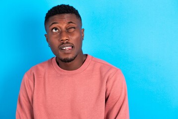 Amazed young handsome man wearing pink sweater over blue background bitting lip and looking tricky...