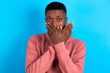 young handsome man wearing pink sweater over blue background shocked covering mouth with hands for mistake. Secret concept.