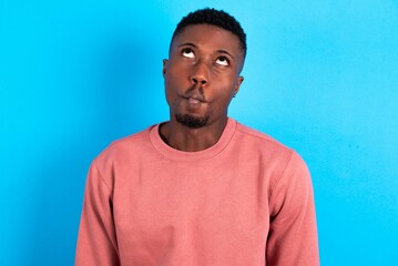 young handsome man wearing pink sweater over blue background making fish face with lips, crazy and...