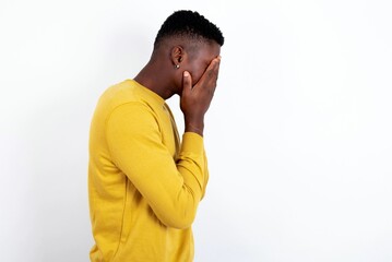 Sad young handsome man wearing yellow sweater over white background covering face with hands and...