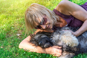 Close-up of a middle-aged blonde woman lying on the grass with her Catalan shepherd dog playing and cuddling. Love for pets. Adoption of animals