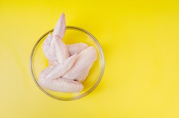 Raw chicken wings in glass bowl isolated on yellow background. Top view. Copy space.