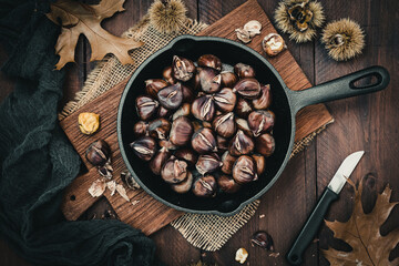 Roasted chestnuts in a cast iron pan on a wooden board