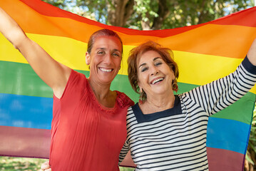 A middle-aged girl next to an older lady raising the gay rainbow flag. Support for the lgbti+, gay, homosexual, bisexual, lesbian, trans, non-binary community. Fight for the freedom and rights