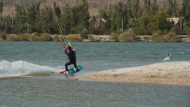 Kiteboarder rides on a kite in sea bay. Freestyle kiter training on pond kiteboarding spot. Kitesurfer enjoying ride. Extreme water sports. Slow motion 120 fps.