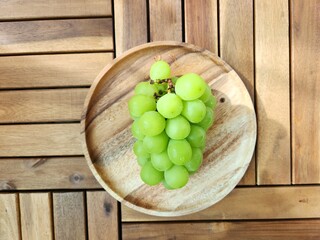large green grapes lie on a wooden plate. Shine Muscat on a wooden plate - on a wooden surface. Korean grapes.