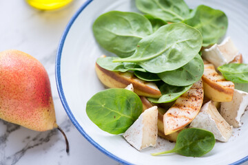 Salad with fresh spinach leaves, grilled pear slices and camembert cheese, close-up, selective focus
