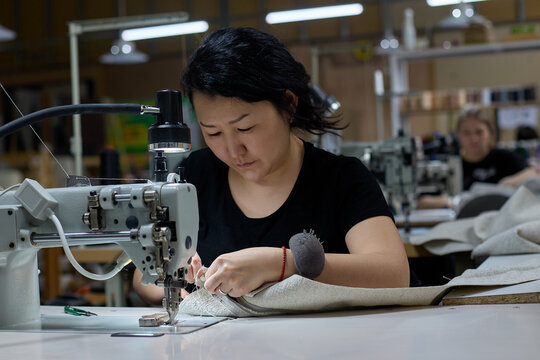 Seamstress or an employee of an Asian textile factory sewing on an industrial sewing machine. The process of sewing from fabric