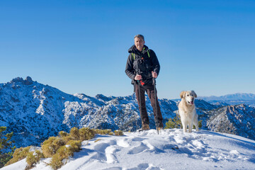 a hiker and his dog pose at the top of snow-capped mountain