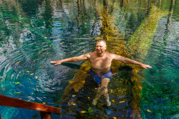 A mature man bathes in a beautiful lake with clear crystal clear turquoise water. Ecotourism. Dominican Republic.