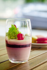 Large transparent glass with cherry dessert, macaron cake on white saucer standing on terrace of cafe, on wooden table