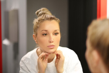 woman looking in the mirror in the bathroom and taking care of her skin.